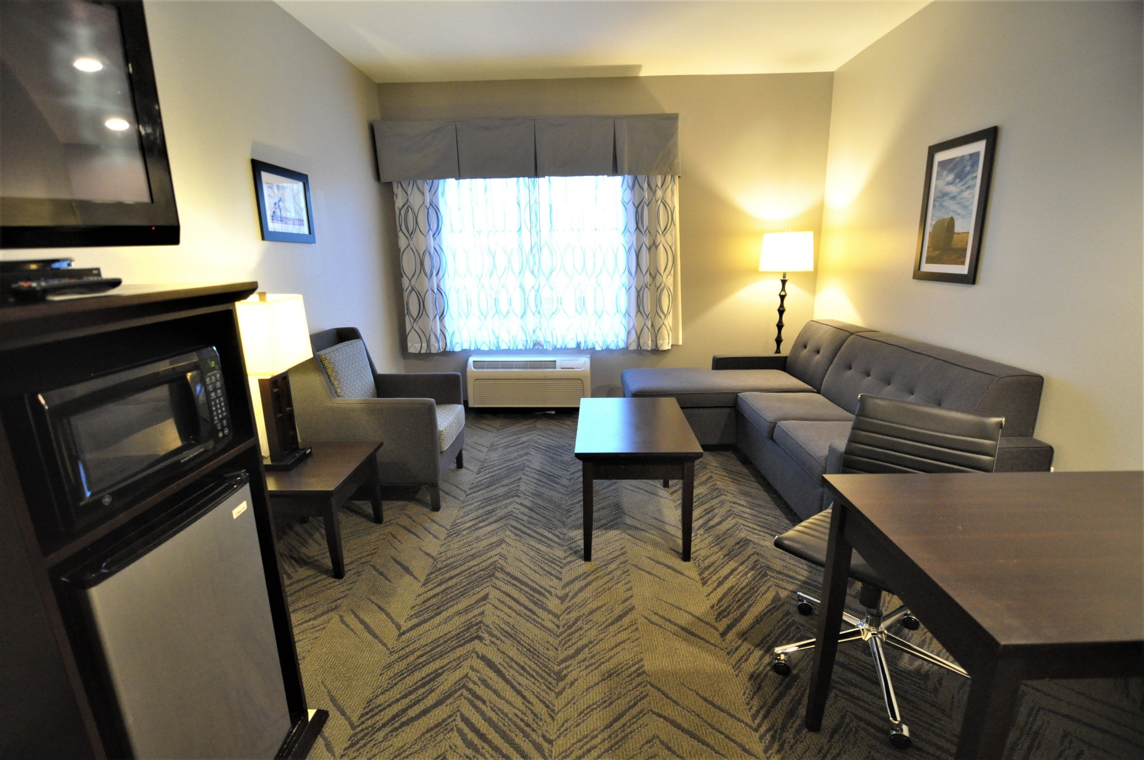 Habitación de hotel con sofá, sillón, mesita y televisor.