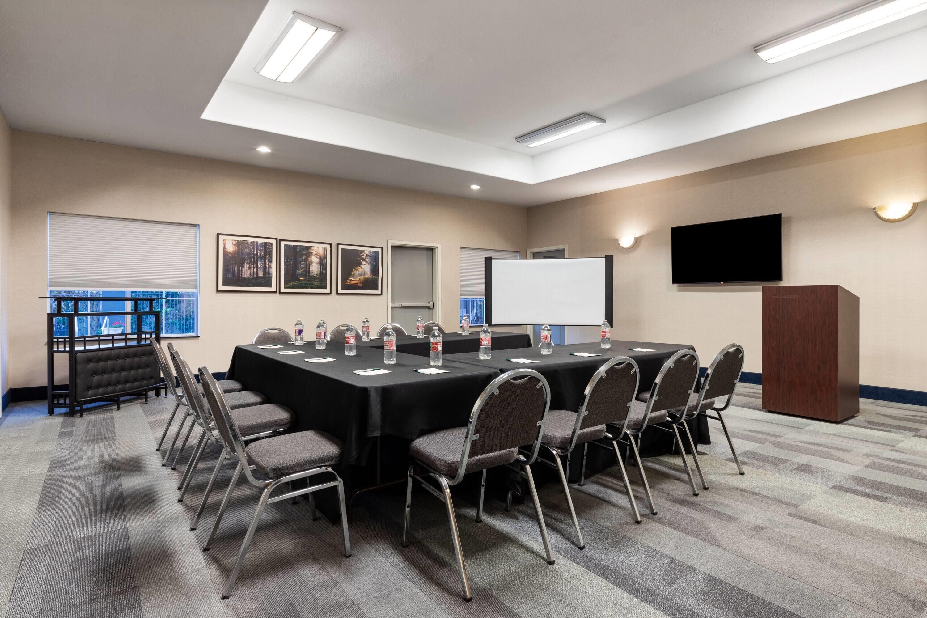 A conference room with a long table, chairs, a projector screen, and a TV.
