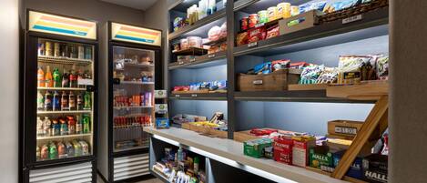 Un quiosco autoservicio para aperitivos y bebidas, con dispensadores de bebidas refrigeradas y estantes llenos de snacks y refrescos.