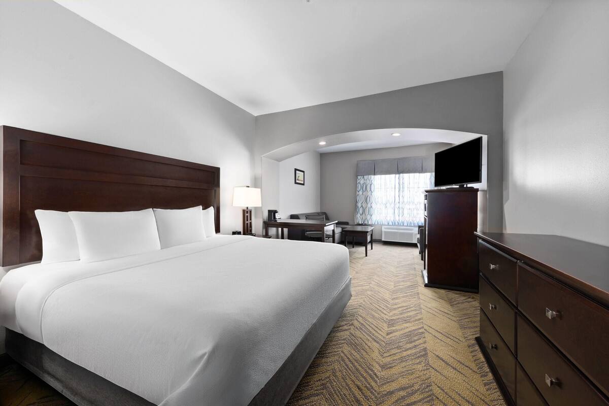 A hotel room with a large bed, a desk, a chair, a dresser, and a television.