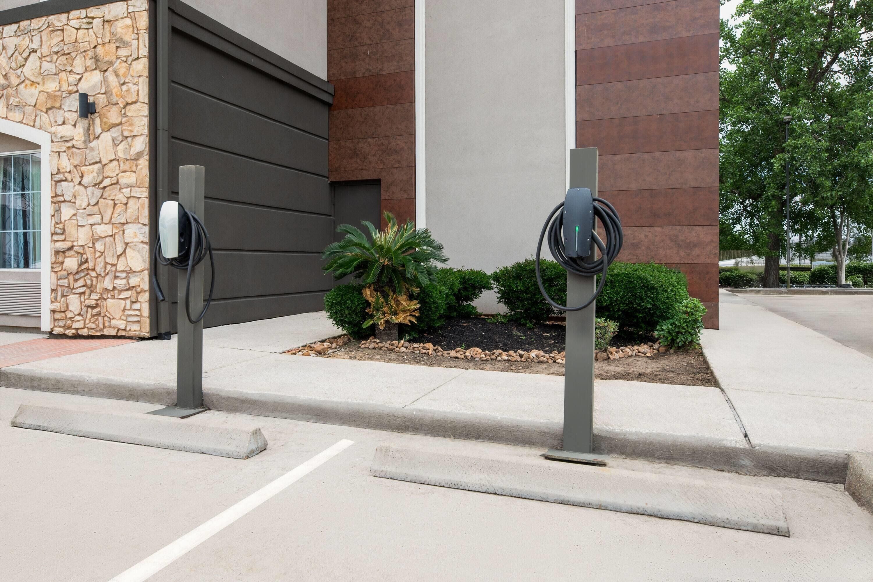 Dues estacions de càrrega per a vehicles elèctrics davant d'un edifici amb façana de pedra i disseny modern.