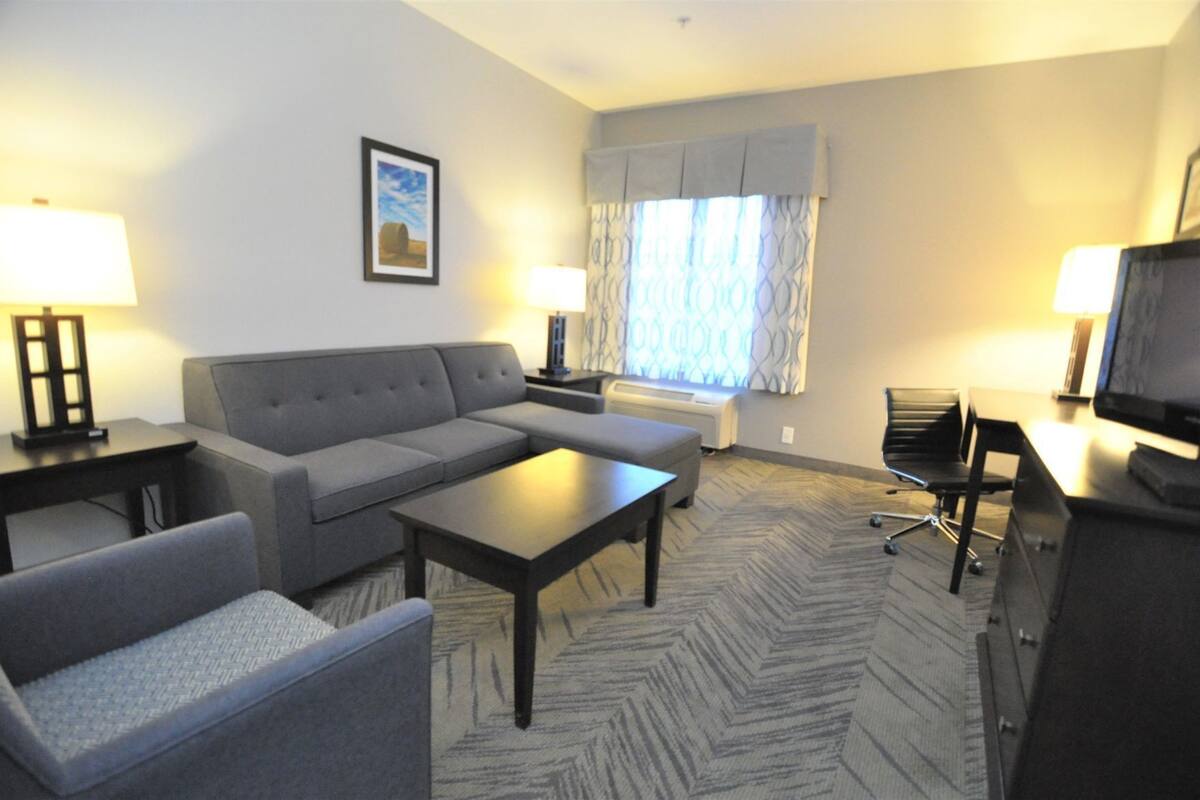 A hotel room with a sofa, a chair, a coffee table, a TV, and a window with curtains.