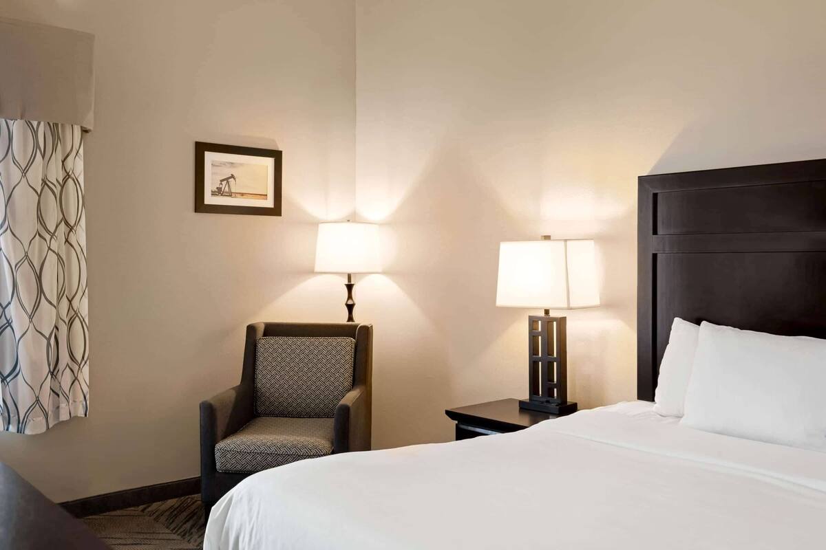 A hotel room with a bed, a chair, two bedside lamps, and a framed picture on the wall.
