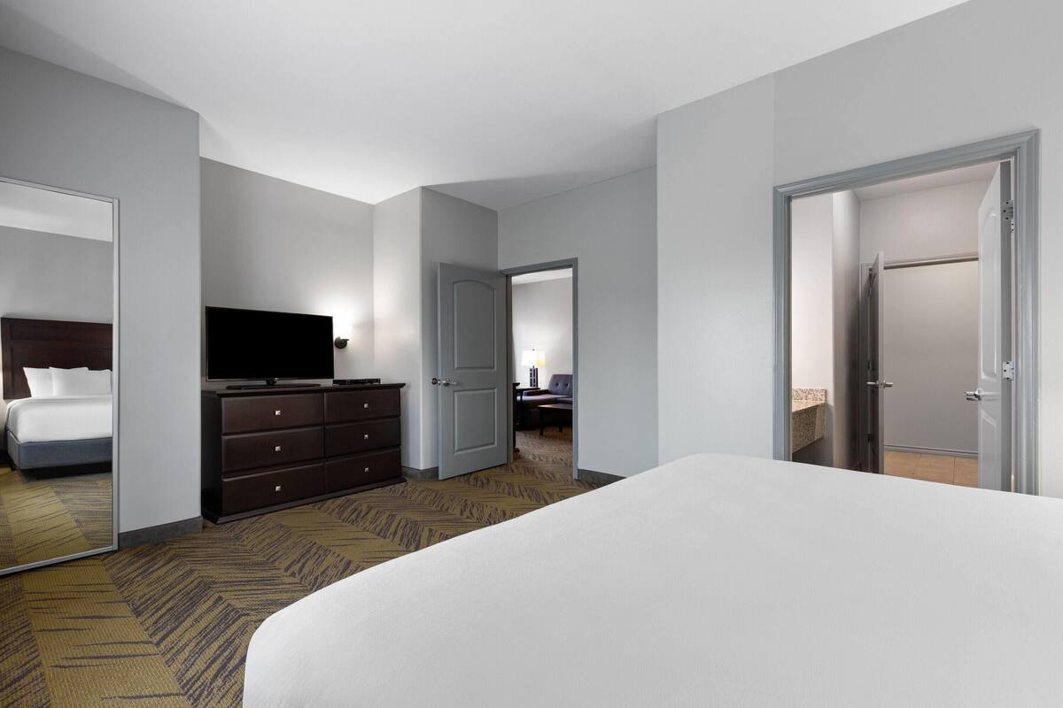 A hotel room with a large bed, a dresser, a flat-screen TV, and a door leading to another room.