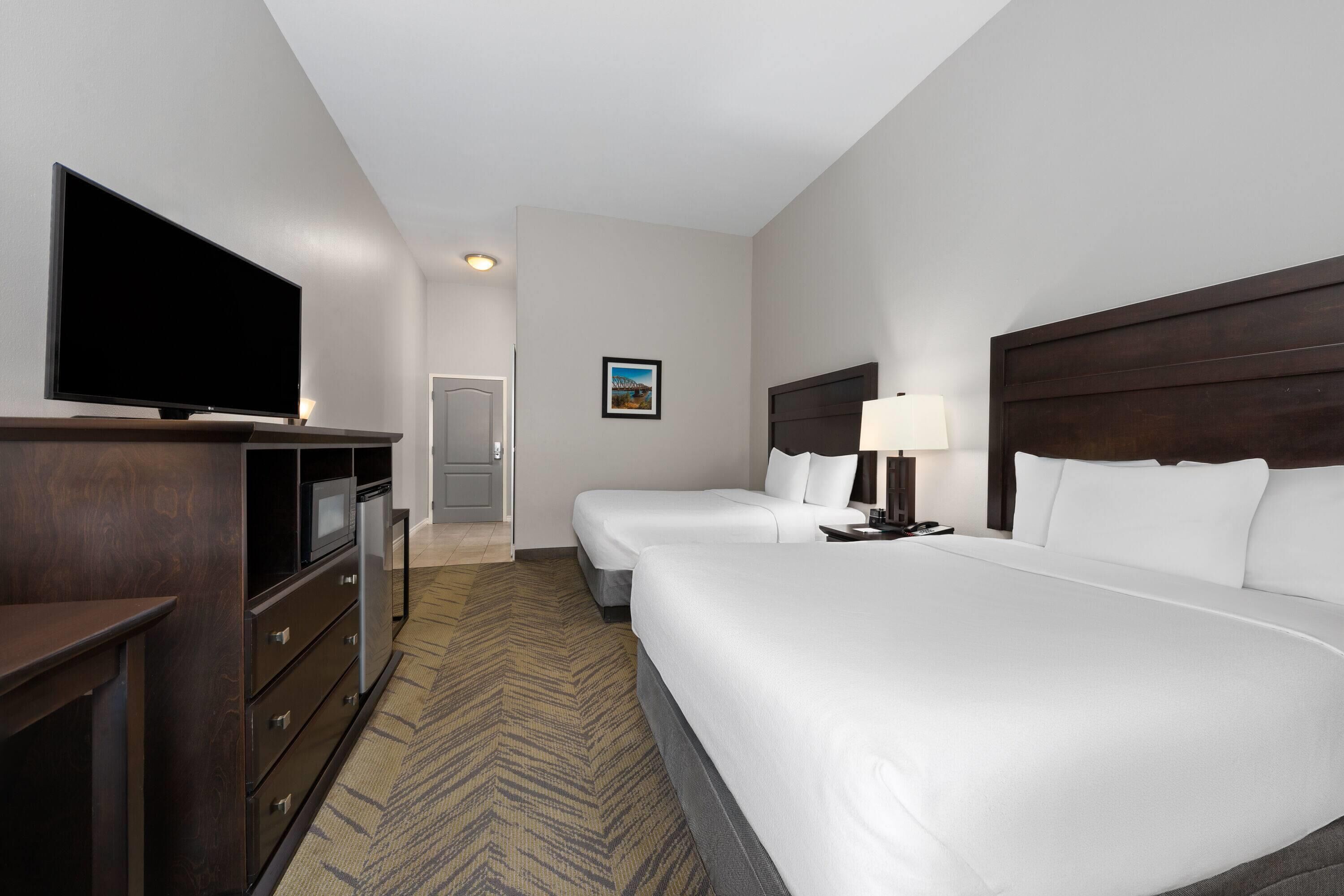A hotel room with a flat-screen TV, a desk with a lamp, two beds, a dresser, and a microwave.