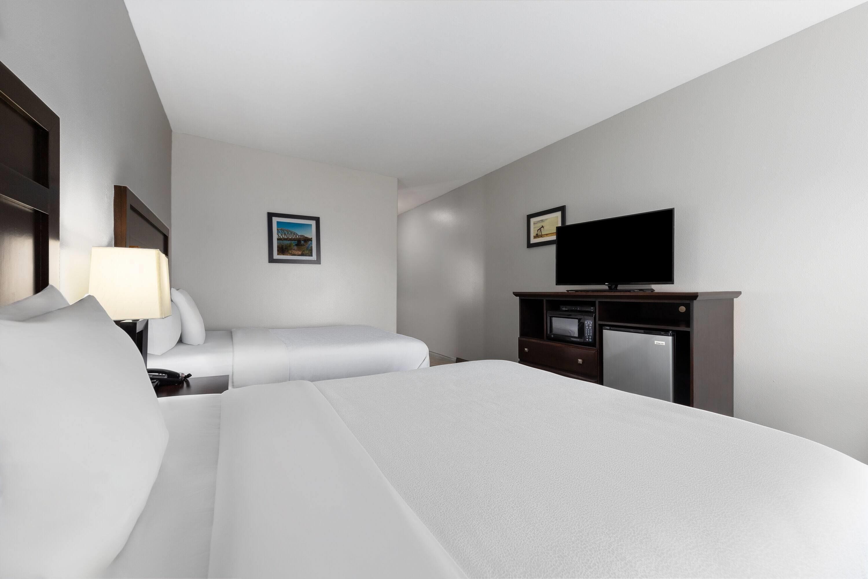 Une chambre d’hôtel avec un grand lit, un bureau doté d’un téléviseur à écran plat, un four à micro-ondes et un petit réfrigérateur. Une fenêtre offre une vue sur un immeuble.