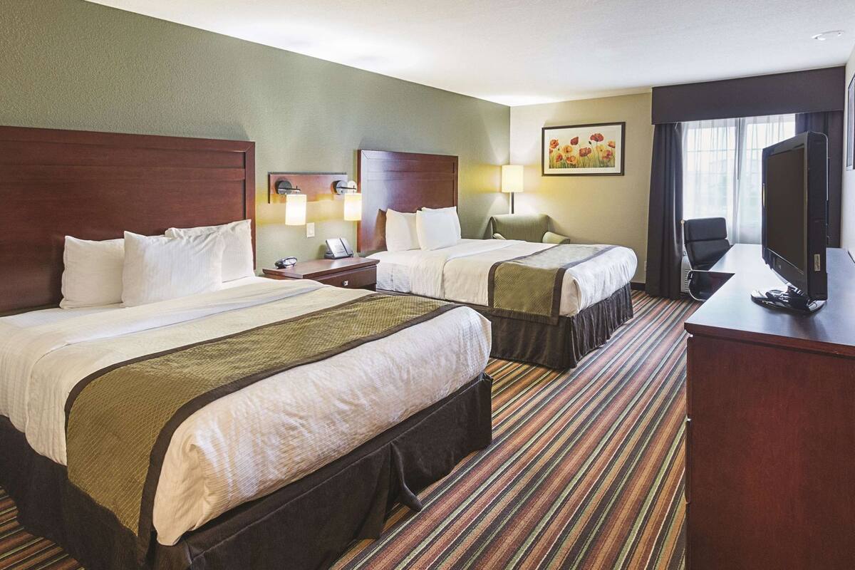 Habitación de hotel con dos camas, un escritorio, un televisor y una ventana con cortinas.