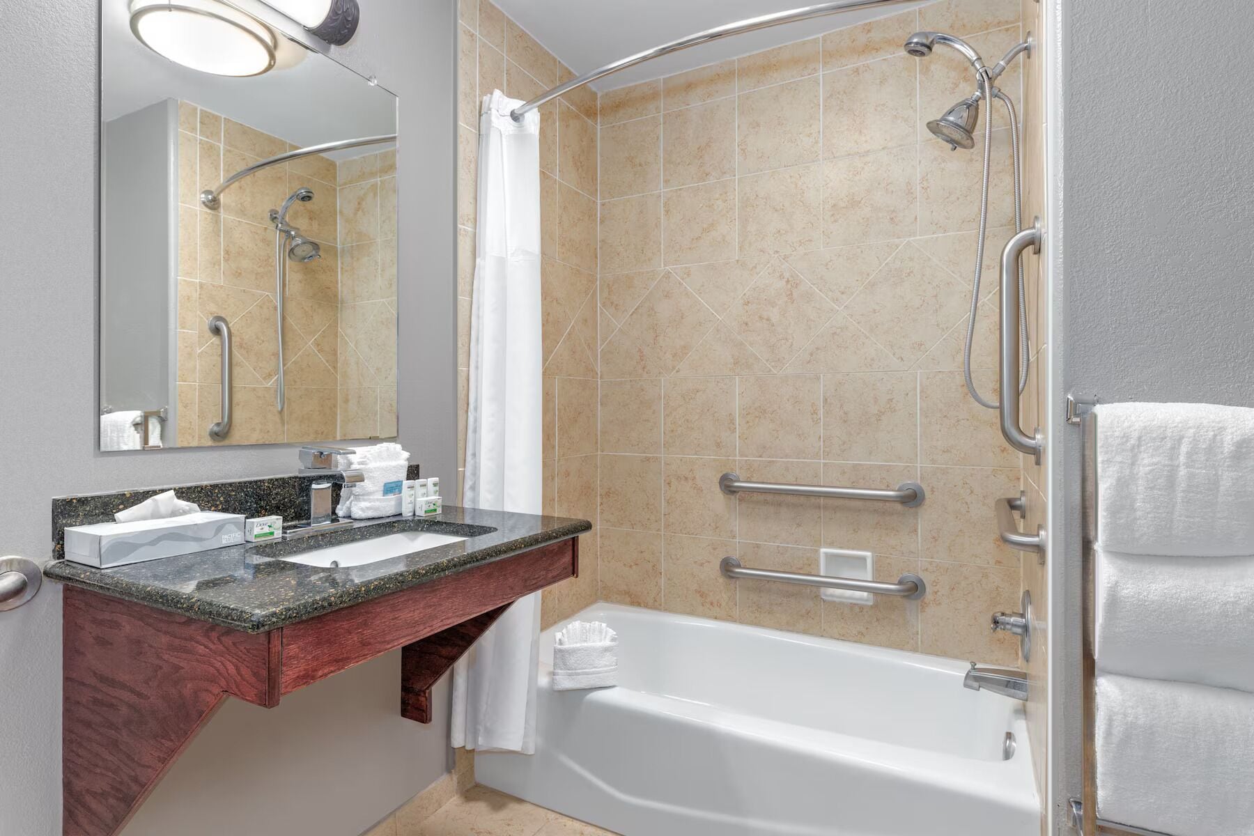 A modern bathroom with a bathtub, a shower with a glass door, a vanity with a granite countertop, and a mirror.