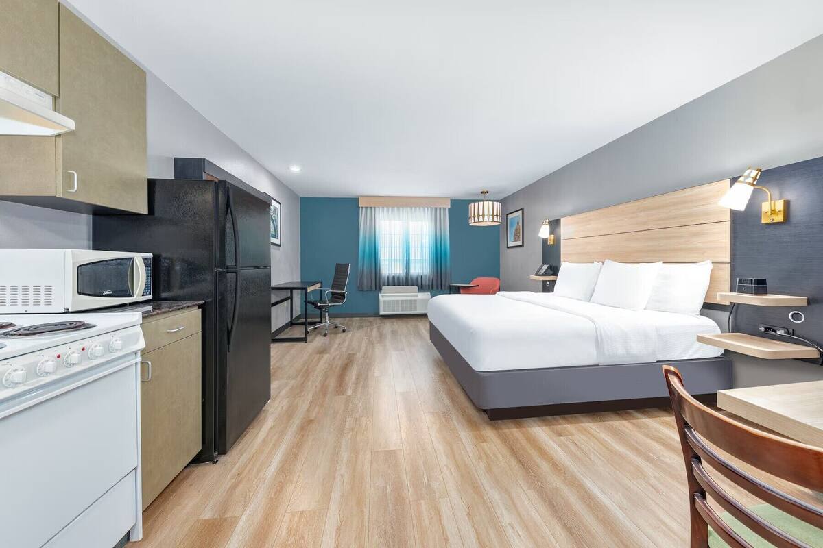 Una habitación de hotel moderna con kitchenette, cama, escritorio y silla.