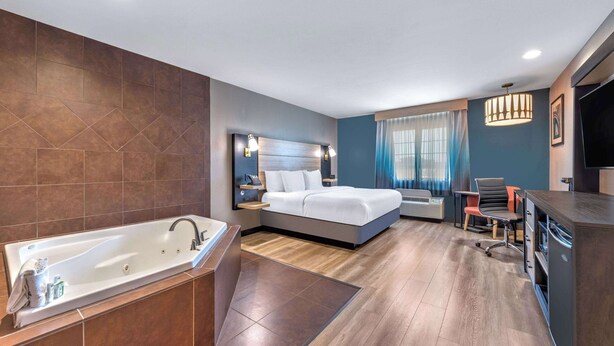 Una habitación de hotel moderna con una bañera grande, una cama con cabecera, un escritorio con silla y una televisión.