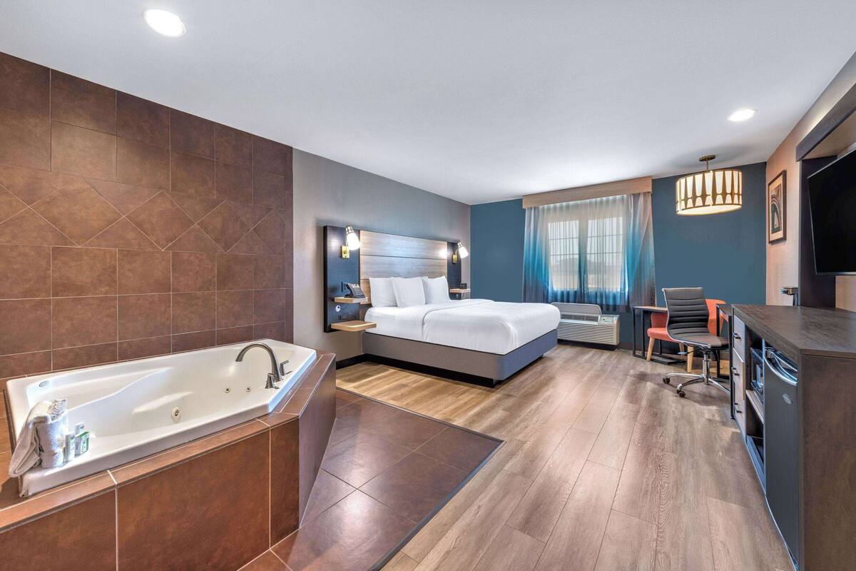 Una habitación de hotel moderna con una bañera grande, una cama con cabecera, un escritorio con silla y una televisión.