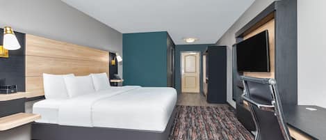 Une chambre d’hôtel moderne, dotée d’un grand lit, d’un bureau, d’une télévision et d’une salle de bain visible à travers une porte ouverte.