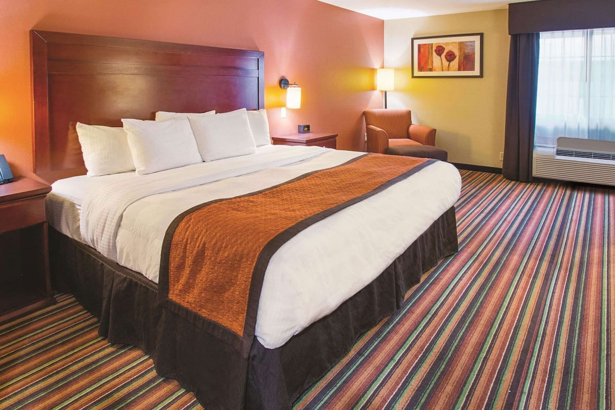 Habitación de hotel con una cama grande, una silla, un escritorio, una lámpara y un cuadro en la pared.