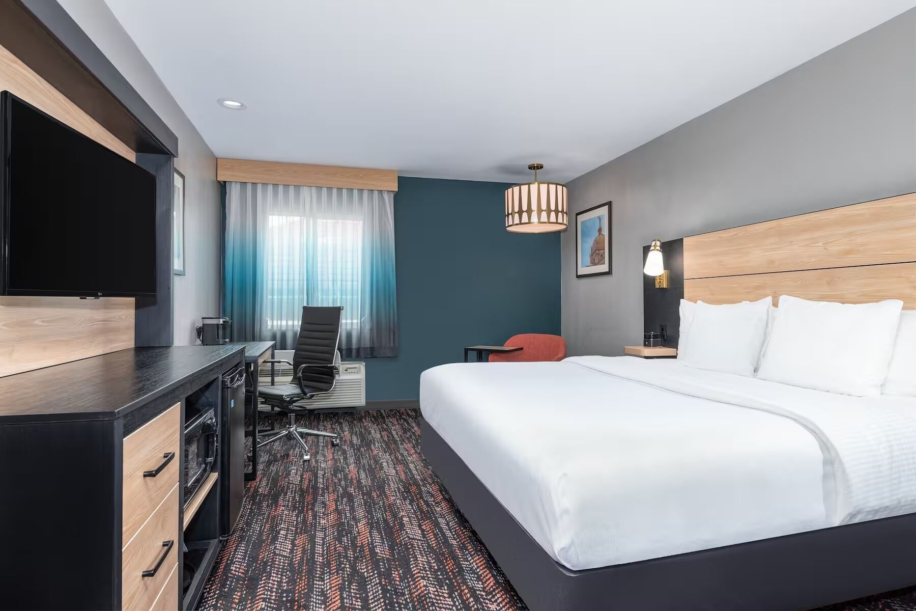 A modern hotel room with a bed, desk, chair, and a TV.