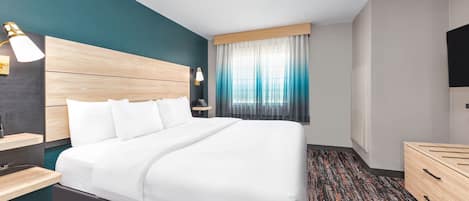 A hotel room with a large bed, a bedside table, a TV, and a window with curtains.