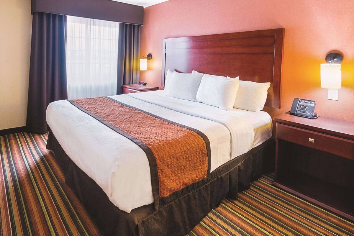 Una habitación de hotel con una cama grande, una mesita de noche con un teléfono, una lámpara y una alfombra a rayas.