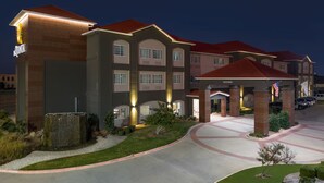 Un hotel de varios pisos con un diseño moderno, que cuenta con una entrada central con un paseo techado y un área de estacionamiento.