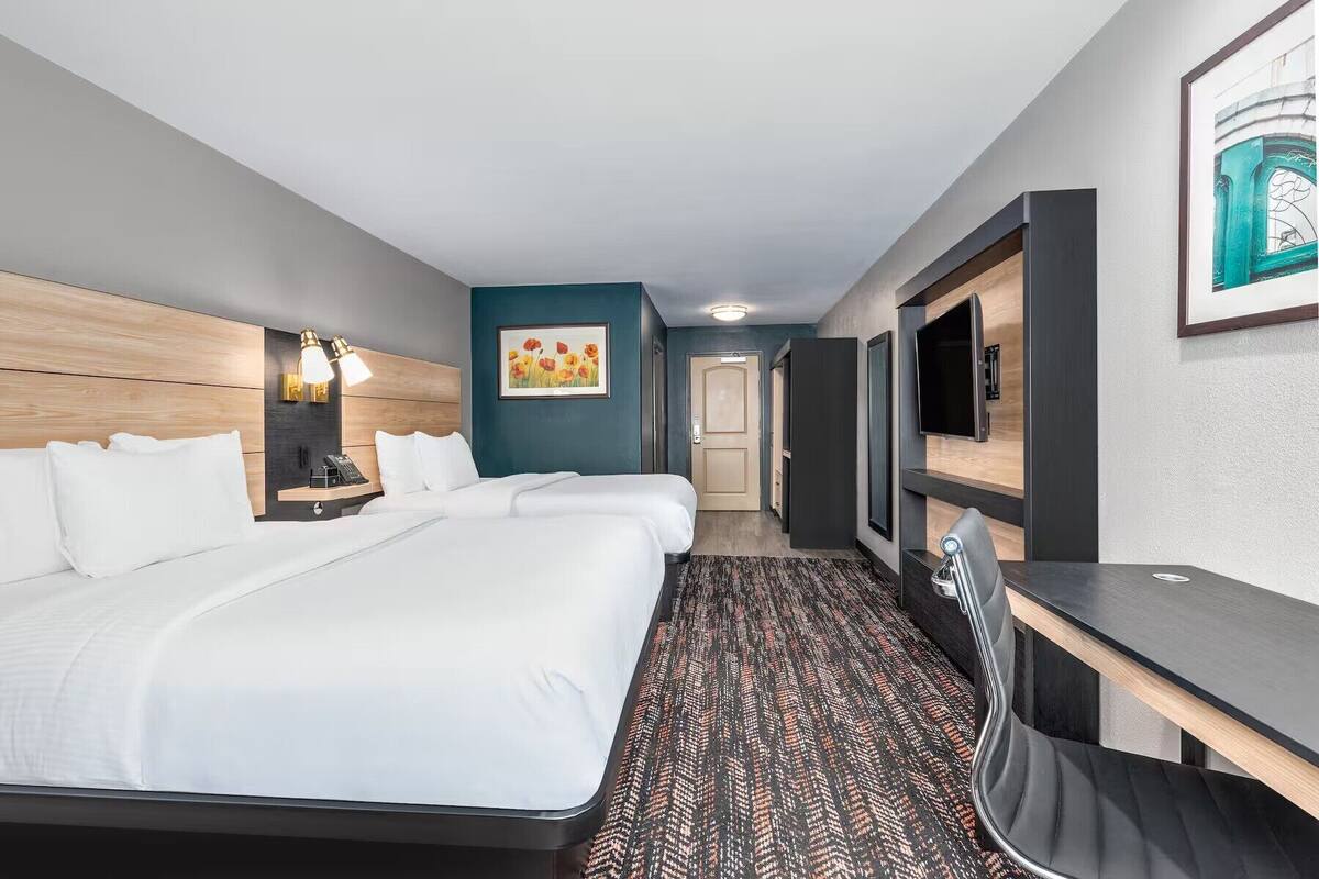 Habitación de hotel con una cama grande, un escritorio, una silla, un televisor y un cuadro en la pared.