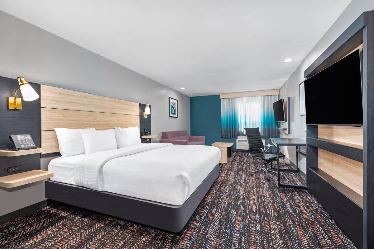 Una habitación de hotel moderna con una cama grande, un escritorio, una silla, un televisor y una ventana con cortinas.