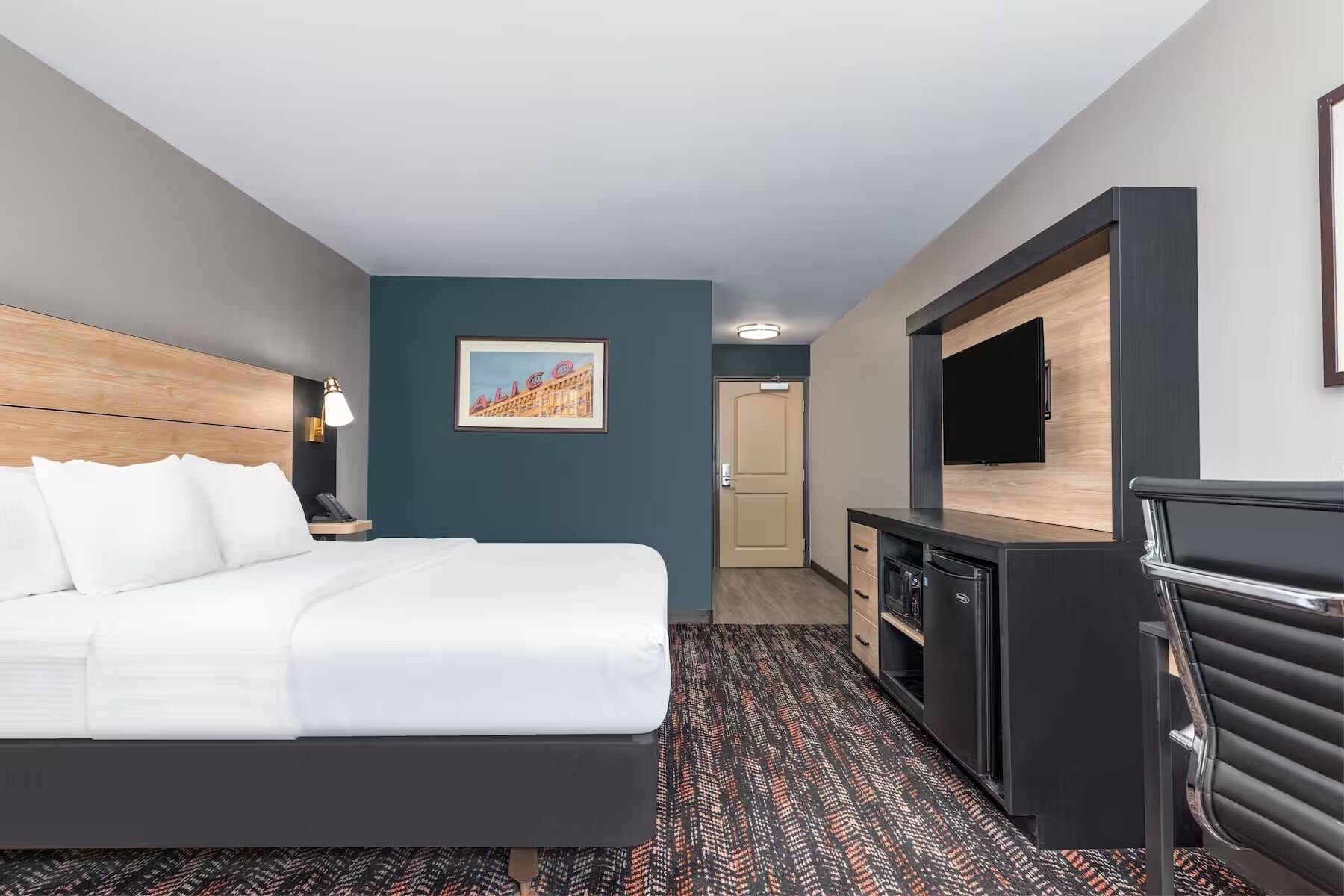 Una habitación de hotel con una cama, un escritorio, un televisor y una puerta que da a otra habitación.