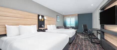 A hotel room with two beds, a desk, a chair, a flat-screen TV, and a window with curtains.