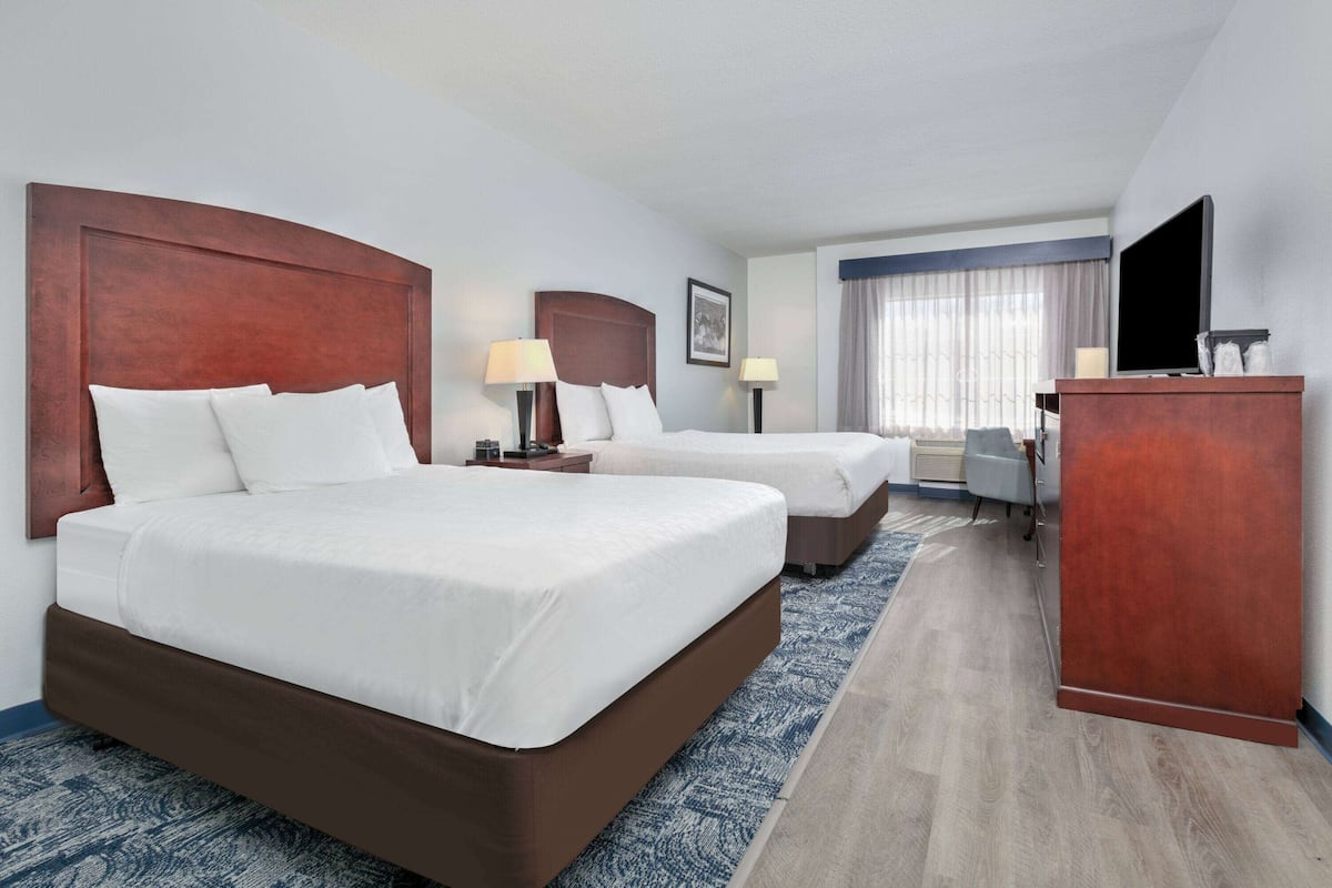Een hotelkamer met twee bedden, een bureau, een televisie en een groot raam met gordijnen.