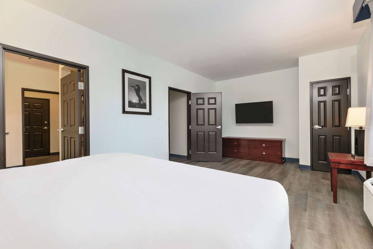 Een hotelkamer met een groot bed, een aan de muur bevestigde televisie, een houten dressoir en twee deuren.
