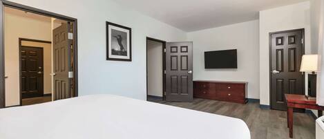 Habitación de hotel con una cama grande, televisor montado en la pared, cómoda de madera y dos puertas.