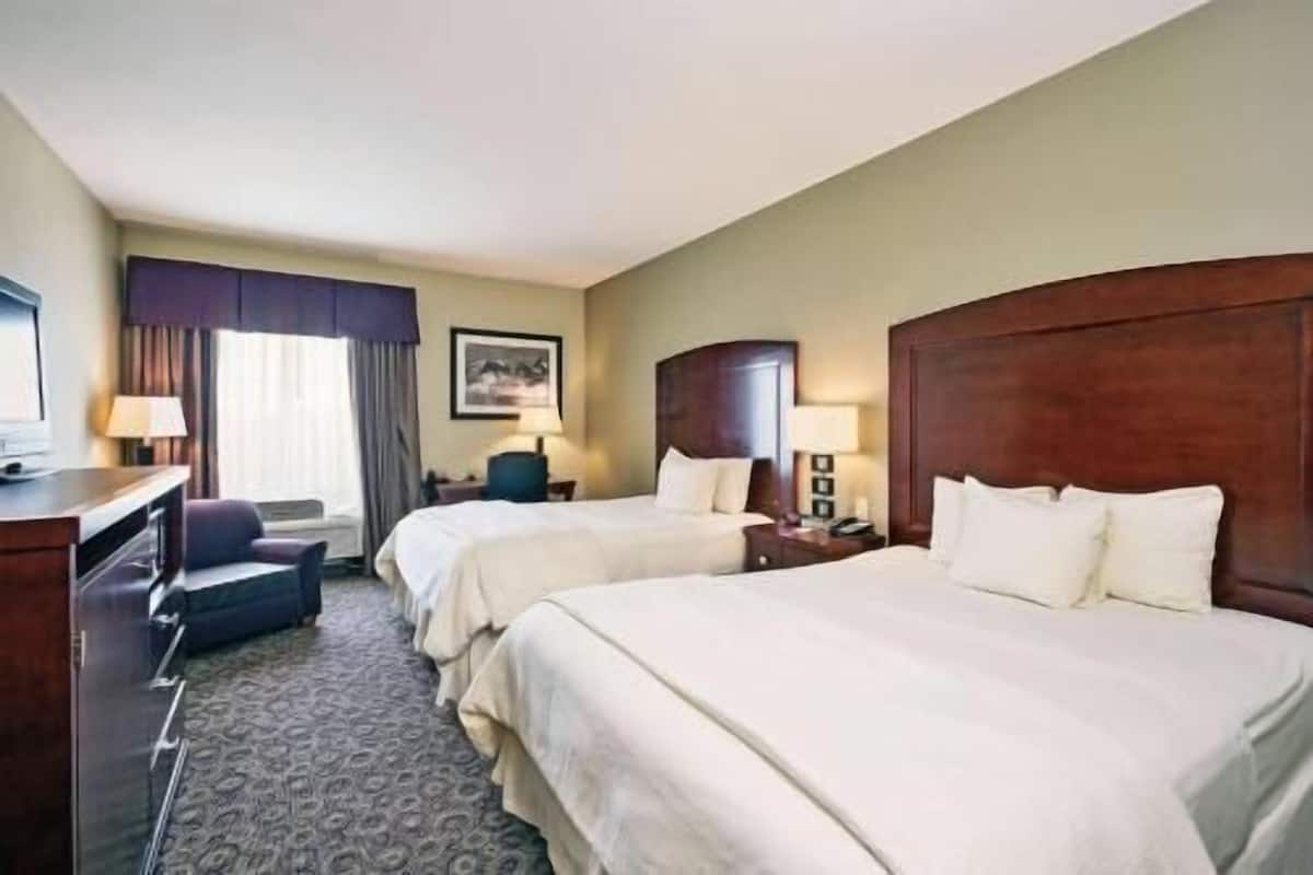 Hotelkamer met twee bedden, een bureau, een stoel, een televisie en een raam met gordijnen.