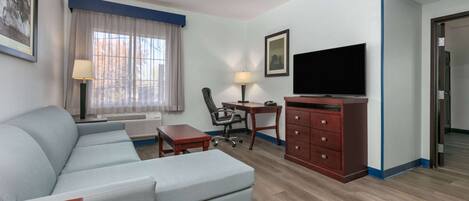A modern hotel room with a sectional sofa, a desk with a chair, a television, and a dresser.