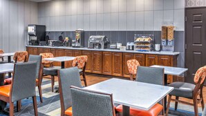 Un comedor de hotel con mesas y sillas, una máquina de café y un mostrador de buffet.
