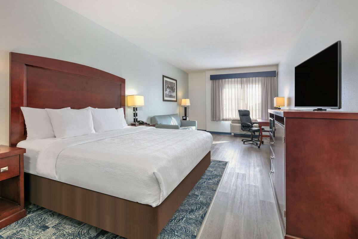 Een hotelkamer met een groot bed, nachtkastjes, een bureau, een stoel, een televisie en een raam met gordijnen.
