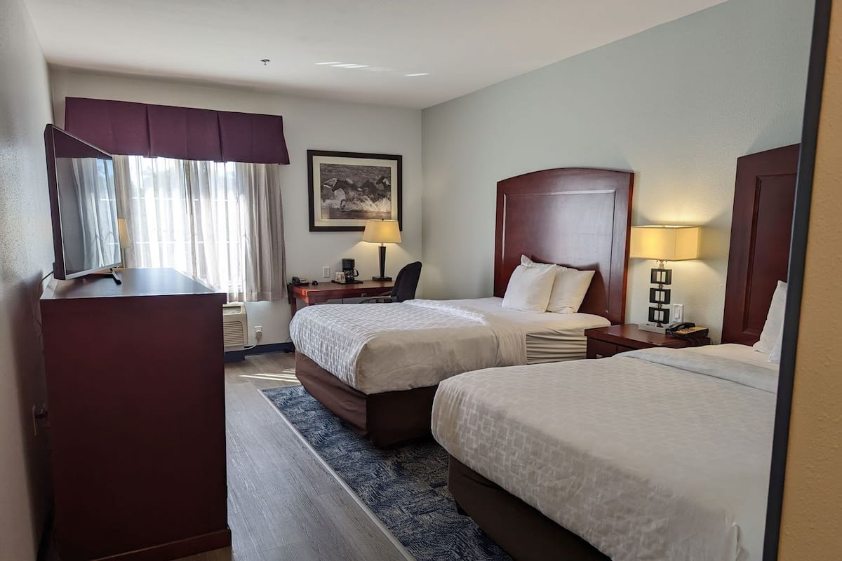 Hotelkamer met twee bedden, een bureau, een stoel, een dressoir en een raam met gordijnen.