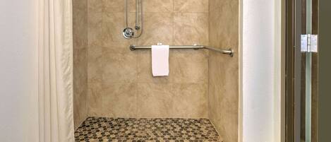 Un área de ducha con azulejos color beige, una puerta de cristal y un perchero para toallas.