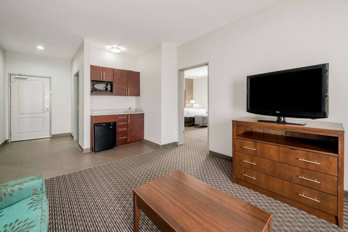 Een hotelkamer met een kitchenette, een televisie, een houten kast en een kamerbreed tapijt met dessin.