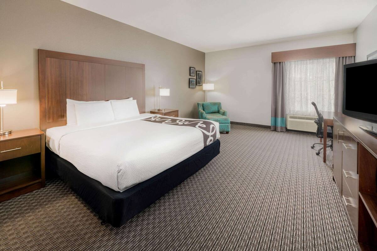 Een hotelkamer met een groot bed, een bureau, een stoel, een televisie en een raam met gordijnen.