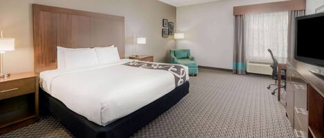 A hotel room with a large bed, a desk, a chair, a TV, and a window with curtains.