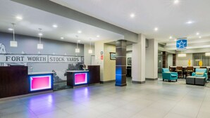 A hotel lobby with a reception desk, seating area, and a sign for 'FORT WORTH STOCK YARDS'.