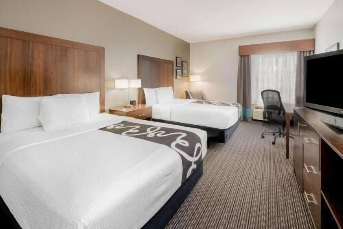 Een hotelkamer met twee bedden, een bureau, een stoel, een televisie en een raam met gordijnen.