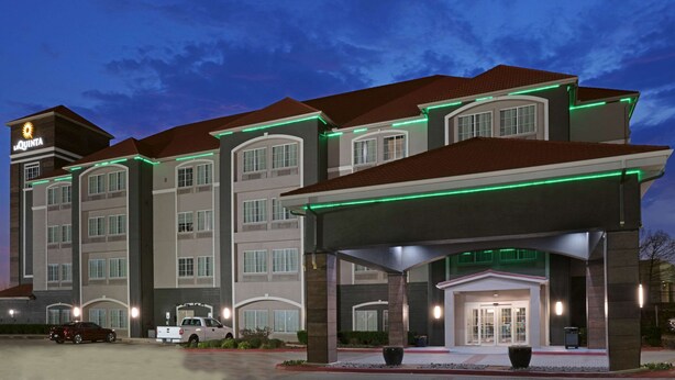 A hotel with a modern design, featuring a prominent entrance with a covered area and a parking lot with several vehicles.