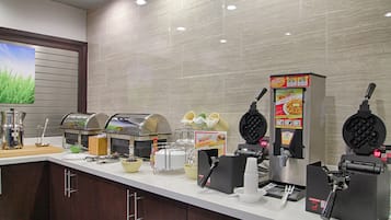 Una barra de desayuno con máquinas para hacer gofres, una máquina de café y diversas opciones para el desayuno.