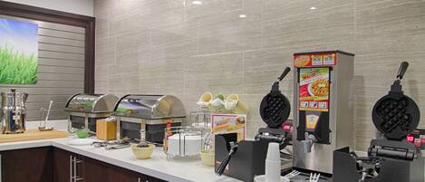 A breakfast bar with waffle makers, a coffee machine, and various breakfast items.