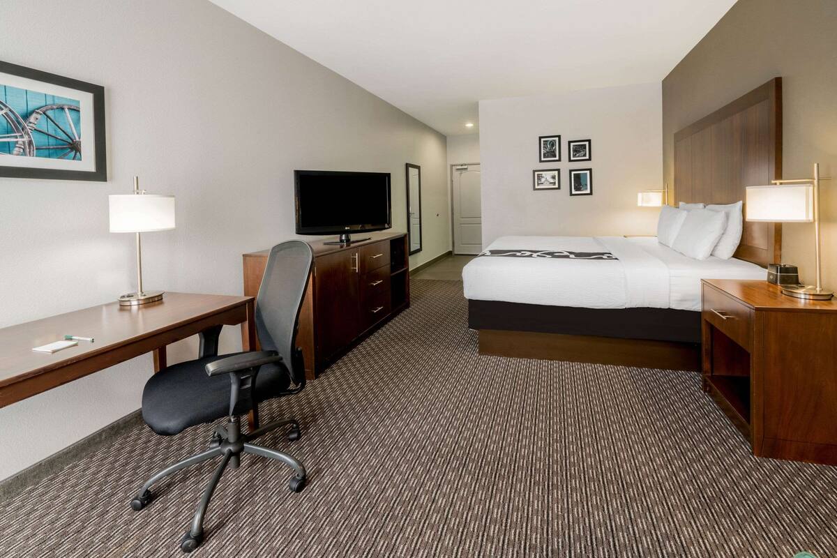 Een hotelkamer met een bed, bureau, stoel, televisie en lampen.