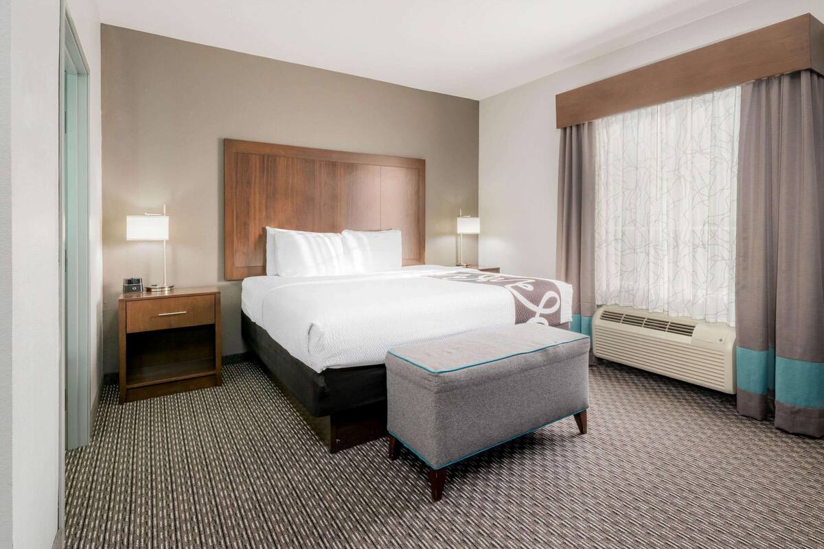 Hotelkamer met een bed, nachtkastjes, een poef, een raam met gordijnen en een wandradiator.