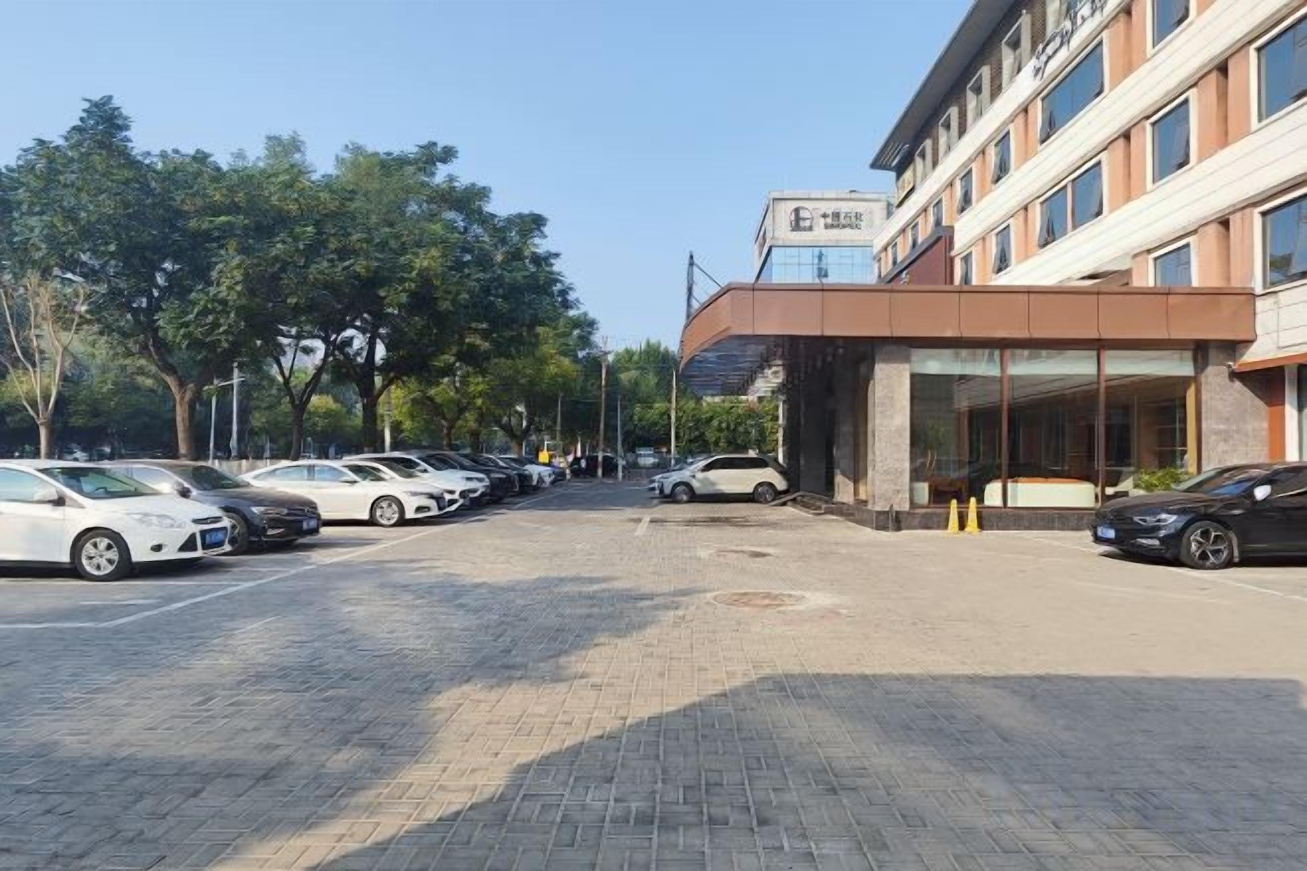 Un estacionamiento con autos, un edificio con un letrero y árboles.