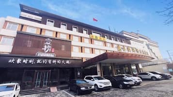 Un hotel de varios pisos, con un letrero llamativo y varios coches aparcados frente a él.