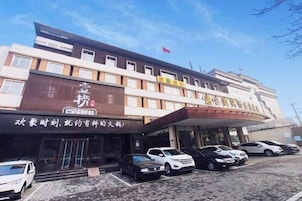 Un hotel de varios pisos, con un letrero llamativo y varios coches aparcados frente a él.