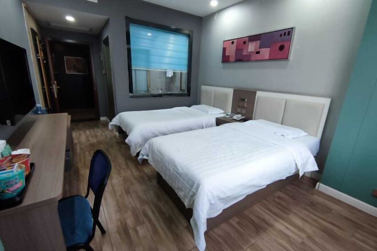A hotel room with two beds, a desk, a chair, and a window with blinds.