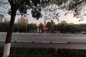 A tree-lined street with a white fence, a red sign, and buildings in the background. - Super 8 Hotel (Xingtai Railway Station Tianyi Square Kaixuan Branch) (Xingtai)