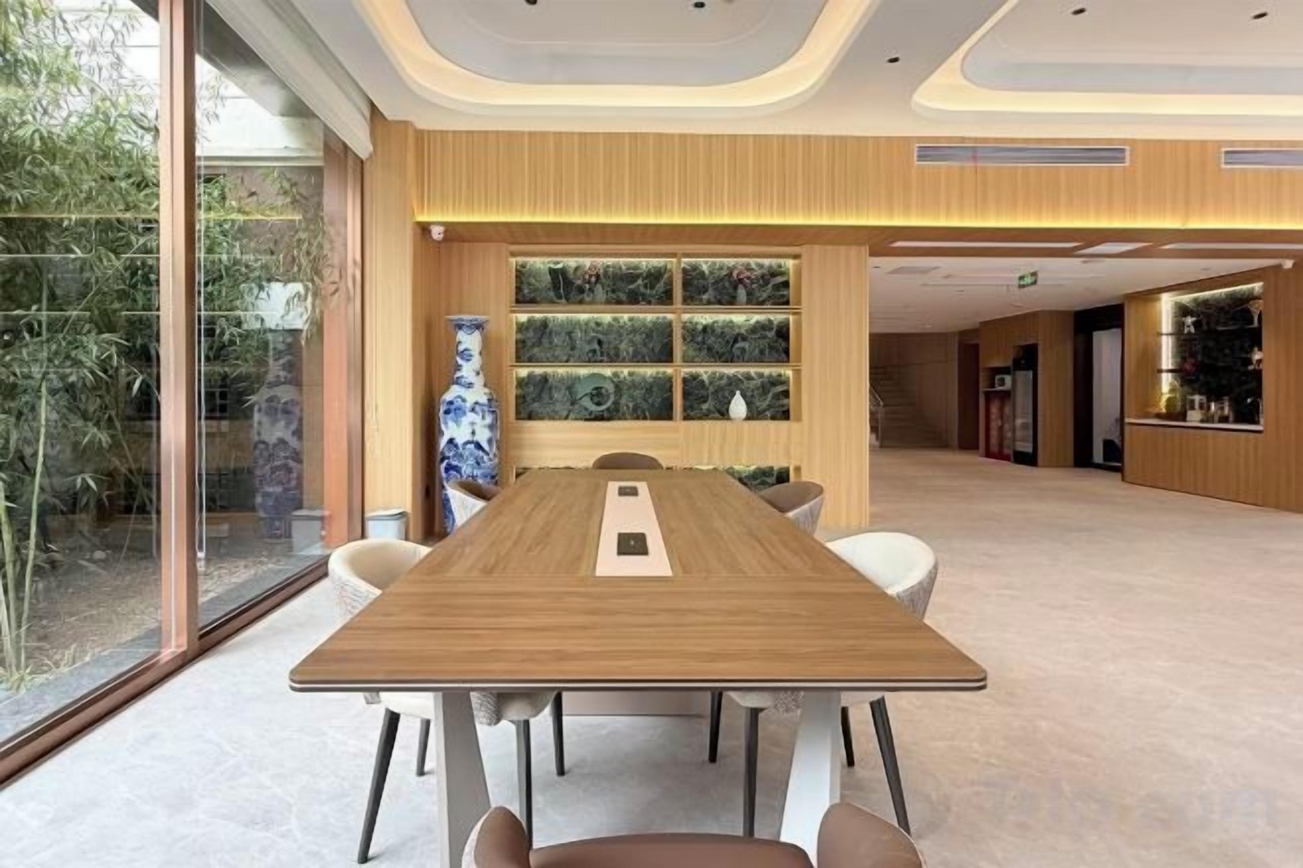 A conference room with a long table, chairs, a vase, and a window with a view of greenery.